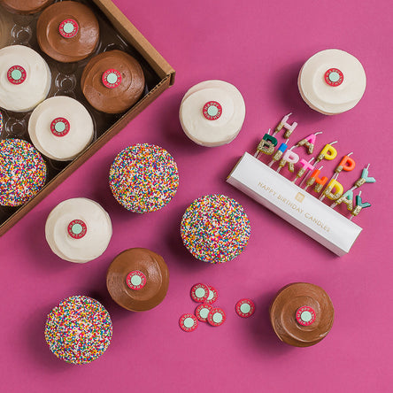 Birthday Box with 12 assorted cupcakes (red velvet, vanilla, dark chocolate, sprinkle), gold candles, decorations, and a birthday sticker.